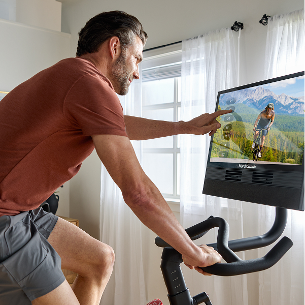 Man following an iFIT cycling class on a NordicTrack S24 during exercise bike workouts at home.